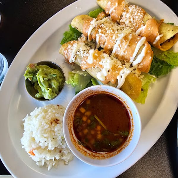Itacate Mexican Food's taquitos with sauce, cheese, guacamole, rice, and a bowl of soup.