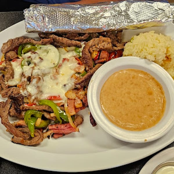 Itacate Mexican Food's steak fajitas with melted cheese, bell peppers, rice, and a side of sauce.