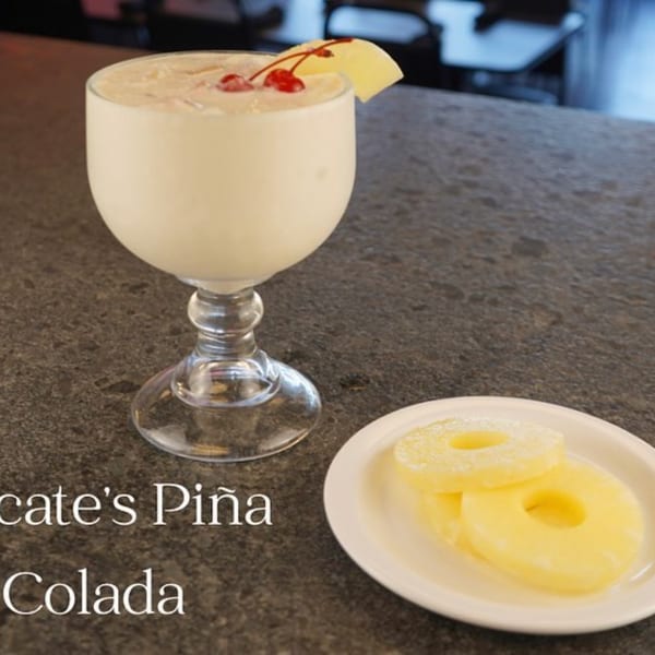Itacate's Piña Colada, garnished with a cherry and pineapple slice, with pineapple rings on the side.