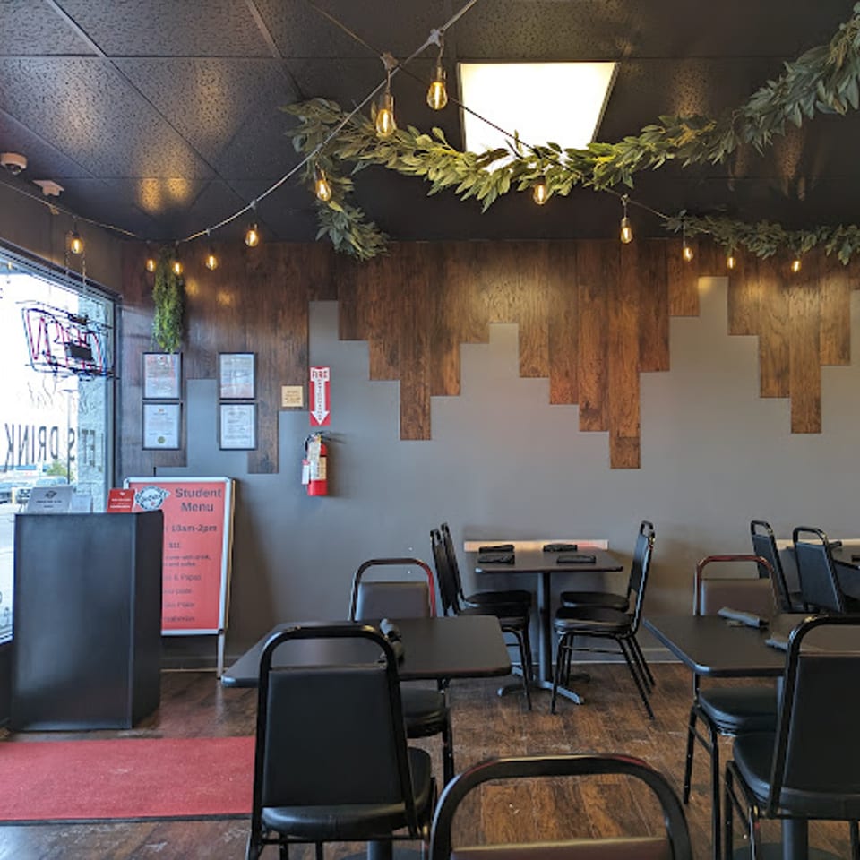 Interior of Itacate Mexican Food, featuring tables, chairs, string lights, and a wooden accent wall.
