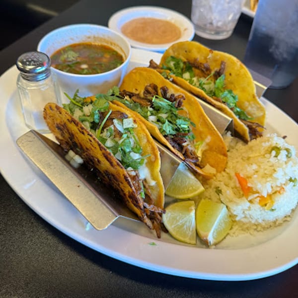 Three Mexican street tacos with cilantro, onions, lime, rice, and a side of soup.