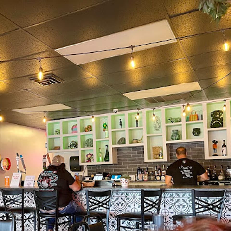 Two men seated at a bar with decorative shelves and string lights at Itacate Mexican Food.