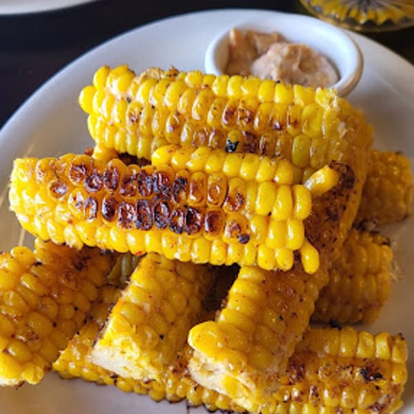 Grilled corn on the cob pieces with char marks, served with a side of sauce.