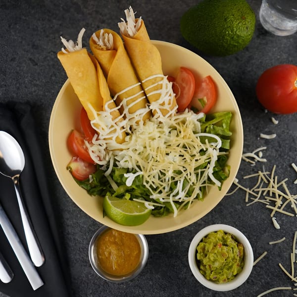Itacate Mexican Food taquitos with shredded cheese, lettuce, tomatoes, lime, guacamole, and salsa.